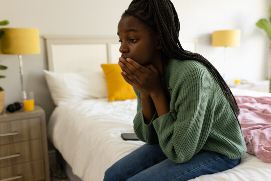 Sad african american teenager girl sitting on bed, covering her face