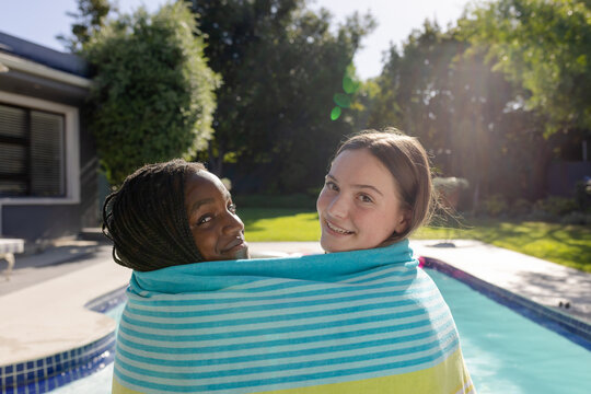 Happy diverse teenager girls friends covered with towel sitting by swimming pool and smiling