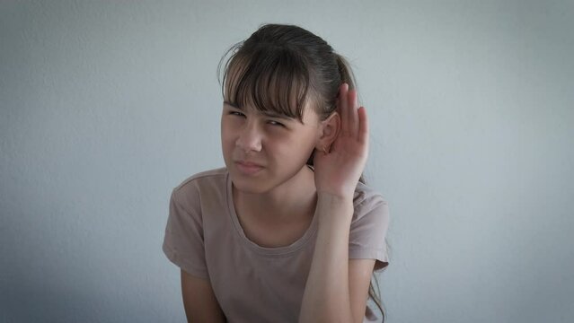 Child with deafness problems indoor. An annoyed upset teen girl keep her hand by the ear for better hearing in the room.