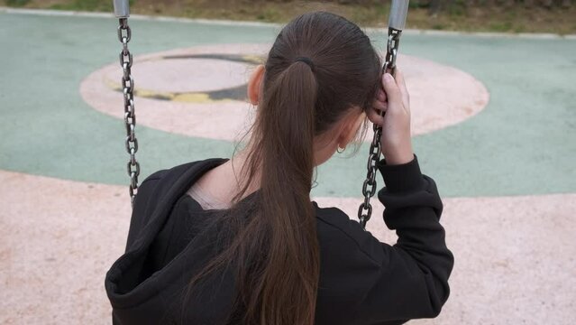 Lost teen on park swing. A view of lost teen girl sitting on swing on empty playground.