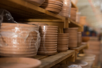 Showcase of home decor shop with stacks of ceramic plates for flower pots packed in polyfilm for sale..