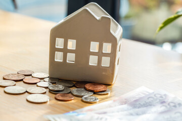 A piggy bank ceramic house next to a lying British coins