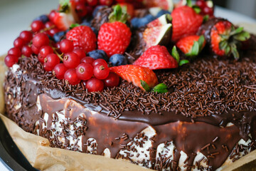 Delicious cake decorated with dark chocolate and fresh figs and blackberries, strawberries, currants. Appetizing chocolate cake with chocolate chips. Advertising for chocolate lovers. Bakery poster