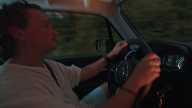 Tired sleepy young man yawns and drives the car on a highway at twilight