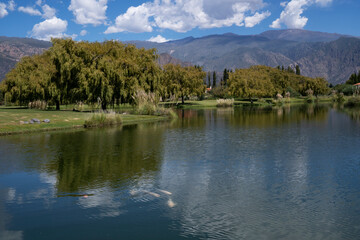 View of the placid artificial lake, carp fishes, trees and mountains in the background, under a...