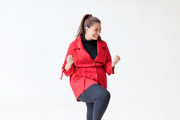 Victorious woman in red coat triumphantly raises fists on white background