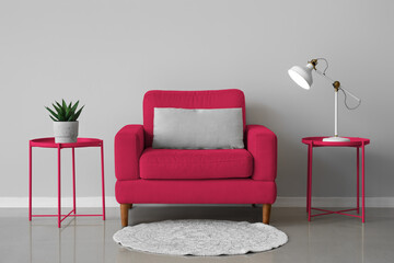 Viva magenta armchair and tables with lamp and houseplant near light wall in room