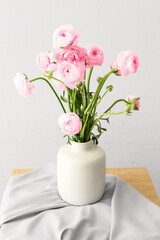 Vase with pink ranunculus flowers on table in room