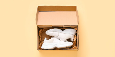 Cardboard box with sports shoes on beige background