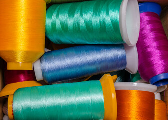 Colored threads in bobbins lie in a box close-up. Textile industry