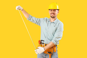 Male carpenter with measure tape on yellow background