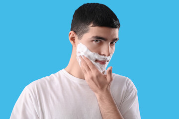 Young man with shaving foam on face against light blue background