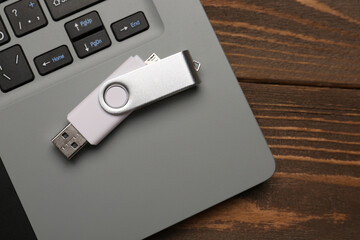 USB flash drive and laptop on wooden background, closeup