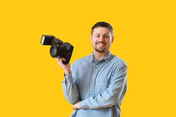 Male photographer with professional camera on yellow background