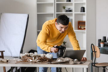 Young male photographer with professional camera using laptop in studio