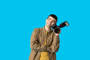 Young male photographer with professional camera on blue background