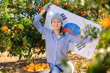 Portrait of a young farmer woman in a fruit nursery, squatting near the collected tangerines and...
