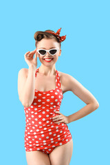 Young pin-up woman in polka dot swimsuit on blue background