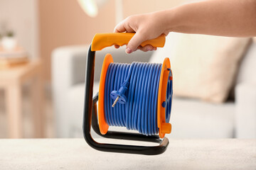 Female hand with extension electric cable reel in room, closeup