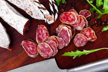 Sliced sausage of dry pork fuet on wooden table with herb.