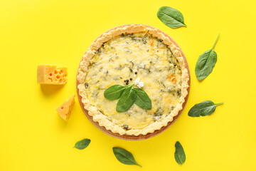 Board with delicious quiche, spinach leaves and cheese on yellow background
