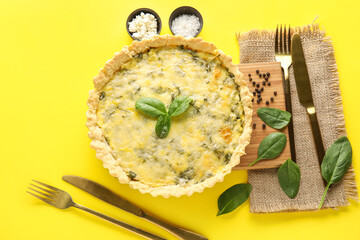 Board with delicious quiche, spinach leaves and cutlery on yellow background