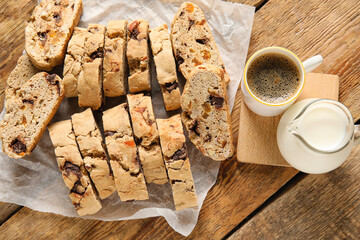 Delicious biscotti cookies, cup of coffee and milk in pitcher on wooden background