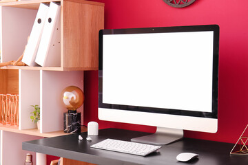 Workplace with computer and earphones near red wall in office