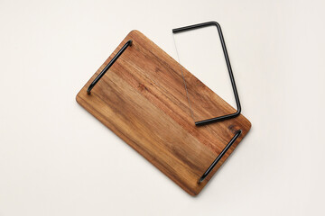 Wooden kitchen board with cheese slicer on light background