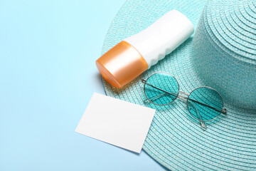 Blank card, sunglasses, hat and bottle of sunscreen cream on color background. Melanoma concept