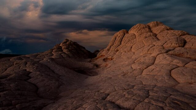 Desert sunset at barren and desolate Arizona and Utah border at white pocket with hard rock petrified hills including timelapse of colorful storm clouds.