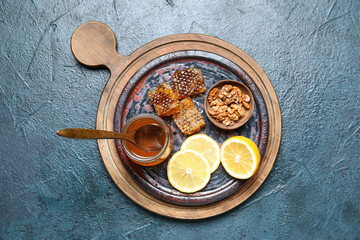 Fototapeta na wymiar Board with jar of honey, lemon slices and nuts on dark background