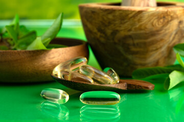 Alternative healthcare and herbal medicine. Fresh herbs, mortar and pestle on a green table. Various herbs and vitamin pills. Close-up, selective focus.