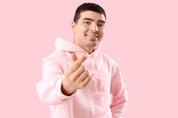 Young man making heart with his fingers on pink background