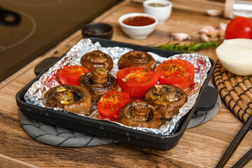 Baking dish with tasty baked mushrooms and tomatoes on wooden table in kitchen