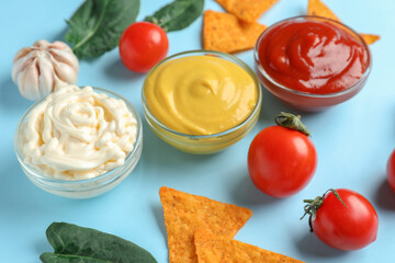 Bowls of different sauces with nachos and vegetables on blue background
