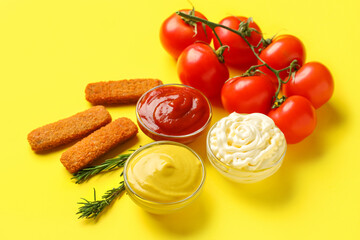 Bowls of different sauces with fish nuggets and vegetables on yellow background