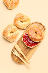 Wooden board of tasty bagels with sesame seeds and strawberry jam on beige background