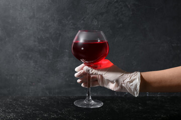 Woman in rubber glove with glass of red wine on dark background