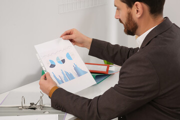 Businessman putting document into punched pocket at white table in office, closeup