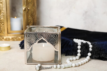 Muslim lamp with burning candle, prayer beads and mat on white table, closeup