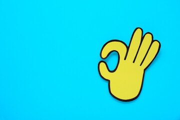 Paper cutout of okay hand gesture on light blue background, top view. Space for text