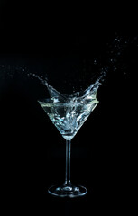 Glass with splashing martini on black background