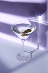 Glass of martini with olives on color background