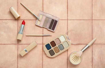 Fototapeta na wymiar Eyeshadows with brushes, powder and lipsticks on beige tile background