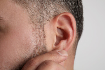 Obraz premium Man touching his ear on light grey background, closeup