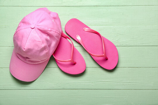 Flip-flops with cap on green wooden background