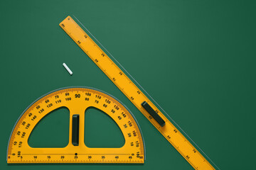 Protractor, ruler and chalk on green chalkboard, flat lay. Space for text