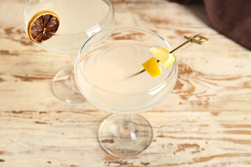 Glasses of martini with lemon on light wooden background