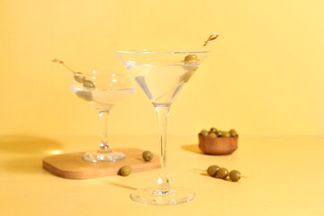 Glasses of martini with olives on yellow background